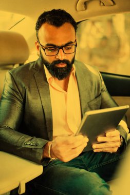 Arka koltukta otururken Tablet bilgisayar/sekme kullanan Hintli/asyalı genç işadamı, seçici odak