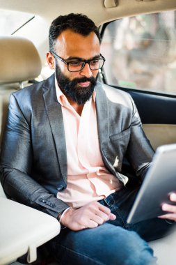 Arka koltukta otururken Tablet bilgisayar/sekme kullanan Hintli/asyalı genç işadamı, seçici odak