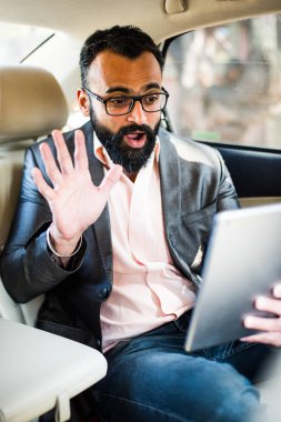 Arka koltukta otururken Tablet bilgisayar/sekme kullanan Hintli/asyalı genç işadamı, seçici odak