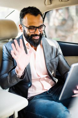 Arka koltukta otururken Tablet bilgisayar/sekme kullanan Hintli/asyalı genç işadamı, seçici odak