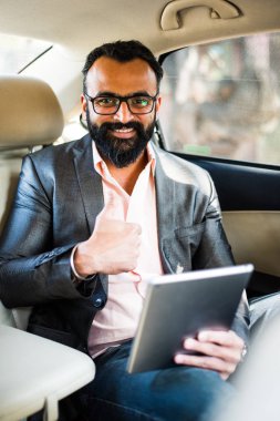 Arka koltukta otururken Tablet bilgisayar/sekme kullanan Hintli/asyalı genç işadamı, seçici odak