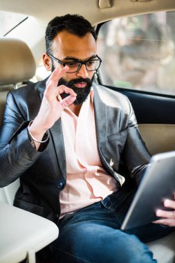 Arka koltukta otururken Tablet bilgisayar/sekme kullanan Hintli/asyalı genç işadamı, seçici odak