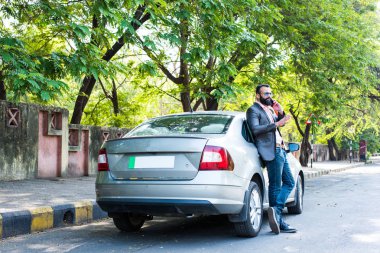 Hint / asyalı genç işadamı arabanın yakınında akıllı telefon kullanarak, dış görünüm. seçici odaklama