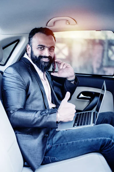 Araba içinde dizüstü bilgisayar ve telefon kullanarak Hint / asyalı genç işadamı, seçici odak