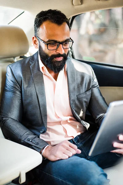 Arka koltukta otururken Tablet bilgisayar/sekme kullanan Hintli/asyalı genç işadamı, seçici odak