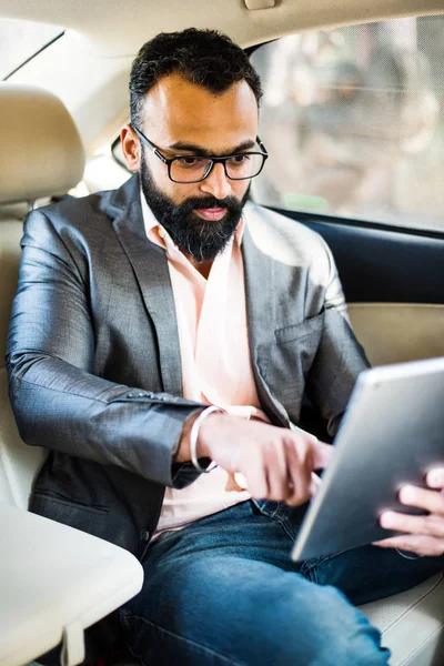 Arka koltukta otururken Tablet bilgisayar/sekme kullanan Hintli/asyalı genç işadamı, seçici odak