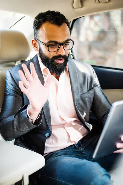 Arka koltukta otururken Tablet bilgisayar/sekme kullanan Hintli/asyalı genç işadamı, seçici odak