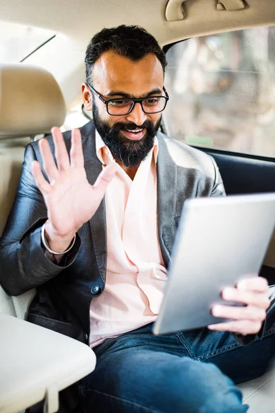 Arka koltukta otururken Tablet bilgisayar/sekme kullanan Hintli/asyalı genç işadamı, seçici odak