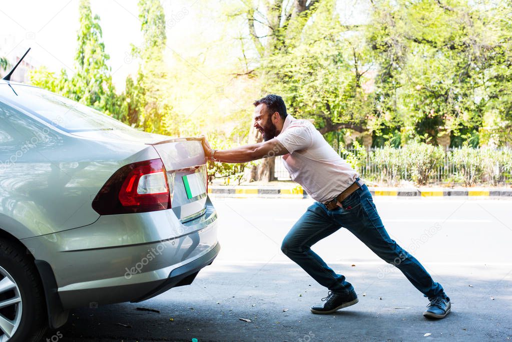 Indian bearded man pushing broken car/vehicle on the road with full force