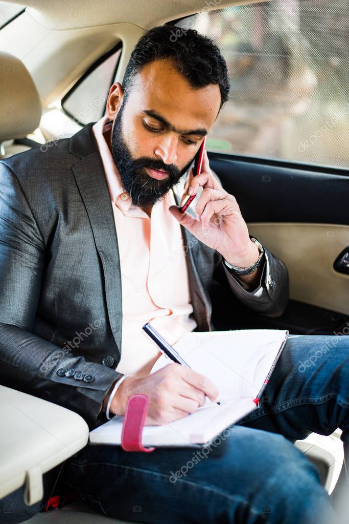 Indian/asian young businessman using smart phone inside the car, selective focus