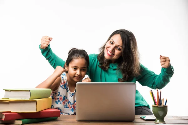 Indian girl studying with mother or teacher at study table with laptop computer, books and having fun learning
