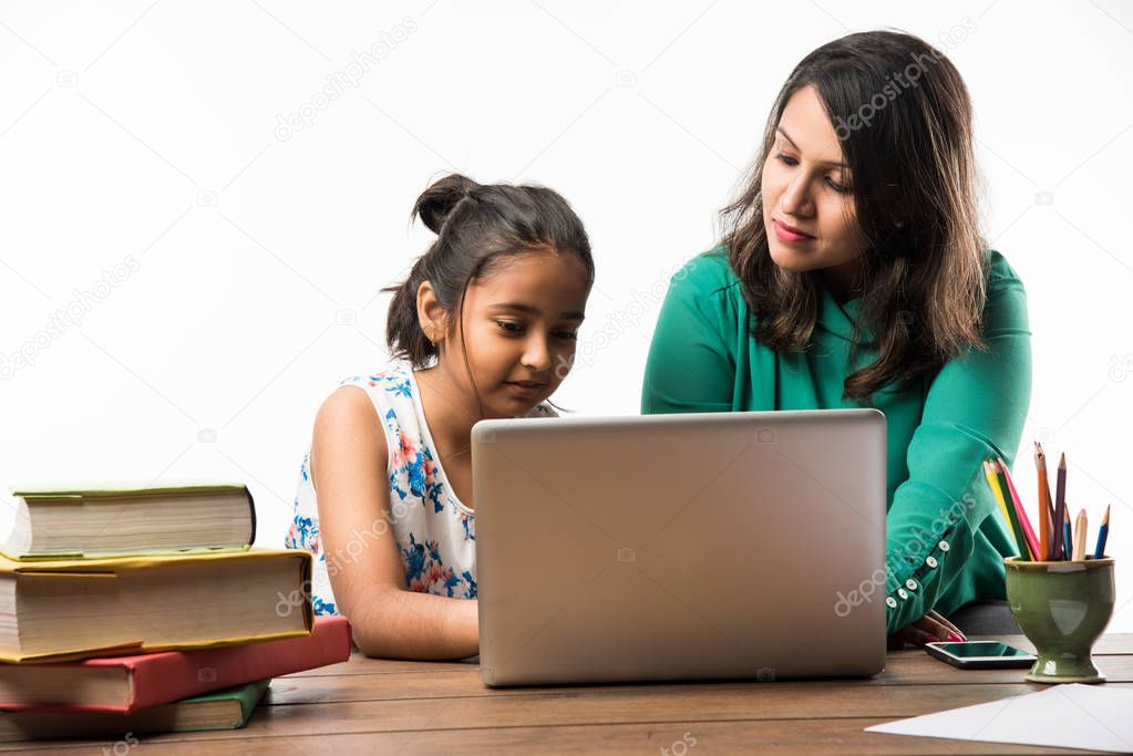 Indian girl studying with mother or teacher at study table with laptop computer, books and having fun learning