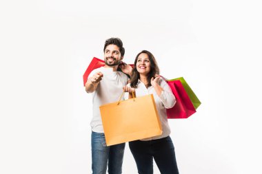 Hintli genç çift alışveriş çantaları ve ödeme için boş banka / kredi veya elektronik kart, beyaz arka plan üzerinde izole ayakta. seçici odaklama