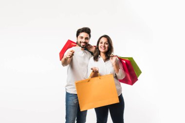 Hintli genç çift alışveriş çantaları ve ödeme için boş banka / kredi veya elektronik kart, beyaz arka plan üzerinde izole ayakta. seçici odaklama