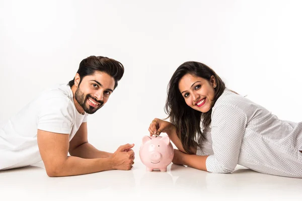 Indian couple with piggy bank lying over white background, side view