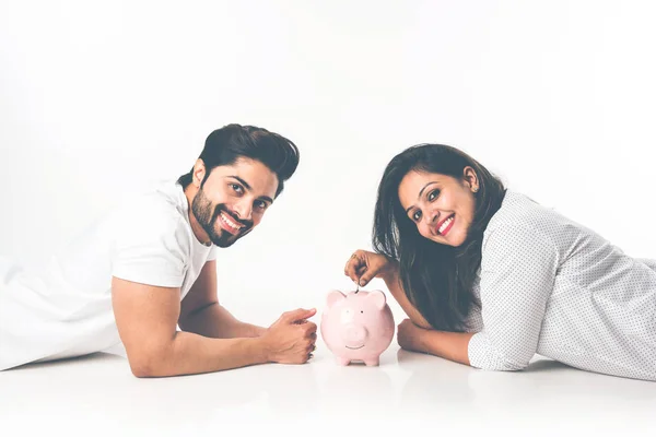 Indian couple with piggy bank lying over white background, side view