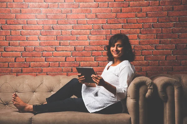 Indian Lady/women using Tablet PC while sitting on sofa/couch, selective focus