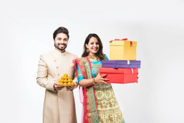 Laddu ve diwali / festival üzerinde hediye kutuları ile Hint çift, beyaz arka plan üzerinde izole ayakta. geleneksel bez giyen