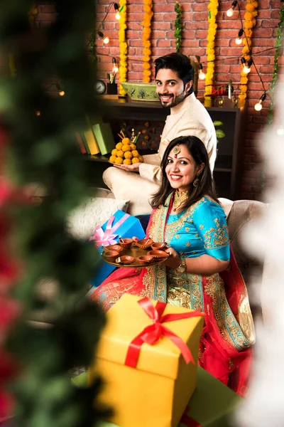 Indian couple with diya, sweets and gifts while celebrating Diwali, Deepavali or Dipavali festival