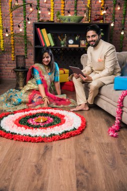 Hintli çift Diwali veya Onam Festivali'nde çiçek Rangoli yapma, selfie alarak veya tatlılar tutarak