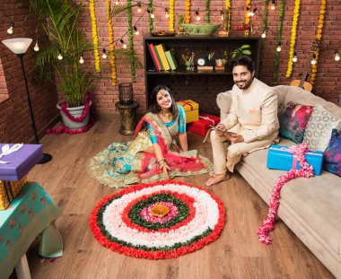 Hintli çift Diwali veya Onam Festivali'nde çiçek Rangoli yapma, selfie alarak veya tatlılar tutarak