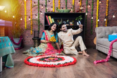 Hintli çift Diwali veya Onam Festivali'nde çiçek Rangoli yapma, selfie alarak veya tatlılar tutarak