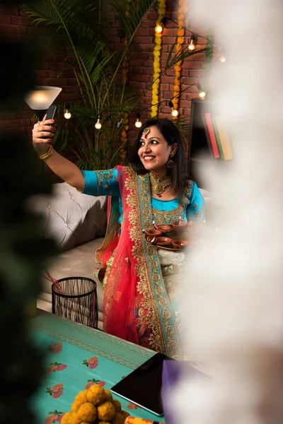 印度女孩拿着迪瓦利迪雅在传统服装 点击自拍图片或说话的智能手机 — 图库照片