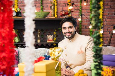 Geleneksel kıyafet giyerken festival gününde tablet dokunmatik bilgisayar kullanan Hintli adam. aydınlatma bokeh ile hediyeler ve tatlılar ile kanepede oturan