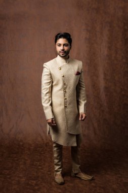 Geleneksel giysili Hintli adam ya da kurta / pijama kumaşlı. Sherwani 'de erkek model, kahverengi grunge arka planına karşı poz veriyor / duruyor, seçici odak noktası