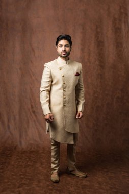 Geleneksel giysili Hintli adam ya da kurta / pijama kumaşlı. Sherwani 'de erkek model, kahverengi grunge arka planına karşı poz veriyor / duruyor, seçici odak noktası