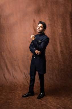 Hintli damat etnik veya geleneksel kıyafetler giyer, koyu mavi sherwani 'li erkek model, kahverengi grunge arka planına karşı poz verir / durur, seçici odak