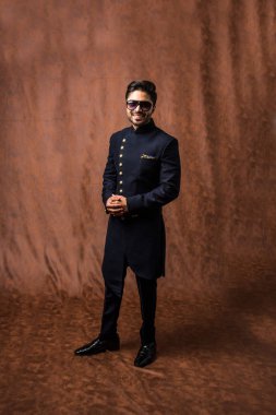Hintli damat etnik veya geleneksel kıyafetler giyer, koyu mavi sherwani 'li erkek model, kahverengi grunge arka planına karşı poz verir / durur, seçici odak