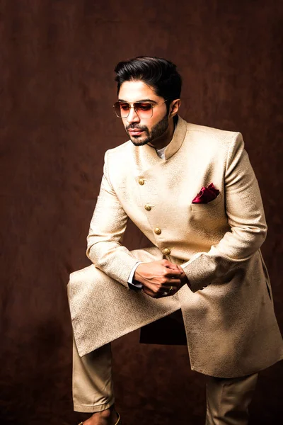 Indian man in traditional wear OR kurta / pyjama cloths.  Male fashion model in sherwani, posing / standing against brown grunge background, selective focus