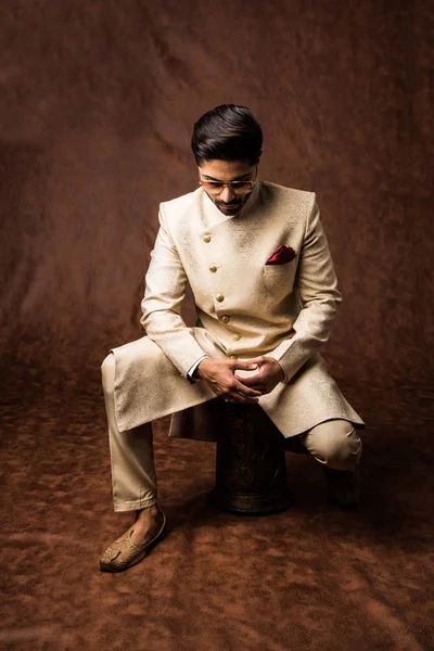 Indian man in traditional wear OR kurta / pyjama cloths.  Male fashion model in sherwani, posing / standing against brown grunge background, selective focus