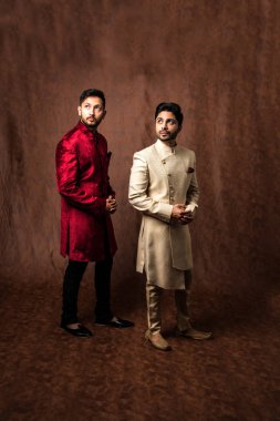 İki Hintli erkek etnik ya da geleneksel kıyafetler giyer, Sherwani ya da Kurta pijamalı erkek modeller, kahverengi grunge arka planında durup poz verirler, seçici bir odak noktası vardır.