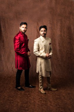 İki Hintli erkek etnik ya da geleneksel kıyafetler giyer, Sherwani ya da Kurta pijamalı erkek modeller, kahverengi grunge arka planında durup poz verirler, seçici bir odak noktası vardır.