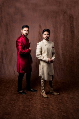 İki Hintli erkek etnik ya da geleneksel kıyafetler giyer, Sherwani ya da Kurta pijamalı erkek modeller, kahverengi grunge arka planında durup poz verirler, seçici bir odak noktası vardır.