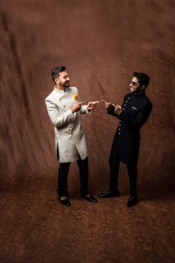 İki Hintli erkek etnik ya da geleneksel kıyafetler giyer, Sherwani ya da Kurta pijamalı erkek modeller, kahverengi grunge arka planında durup poz verirler, seçici bir odak noktası vardır.