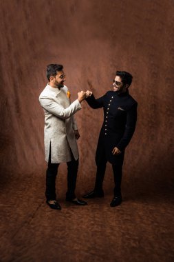 İki Hintli erkek etnik ya da geleneksel kıyafetler giyer, Sherwani ya da Kurta pijamalı erkek modeller, kahverengi grunge arka planında durup poz verirler, seçici bir odak noktası vardır.