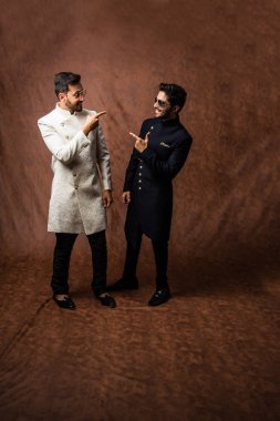 İki Hintli erkek etnik ya da geleneksel kıyafetler giyer, Sherwani ya da Kurta pijamalı erkek modeller, kahverengi grunge arka planında durup poz verirler, seçici bir odak noktası vardır.