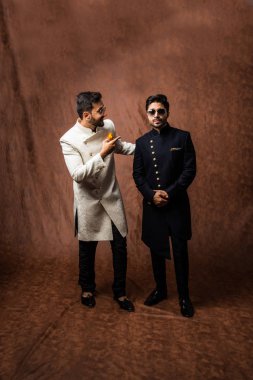 İki Hintli erkek etnik ya da geleneksel kıyafetler giyer, Sherwani ya da Kurta pijamalı erkek modeller, kahverengi grunge arka planında durup poz verirler, seçici bir odak noktası vardır.