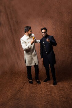 İki Hintli erkek etnik ya da geleneksel kıyafetler giyer, Sherwani ya da Kurta pijamalı erkek modeller, kahverengi grunge arka planında durup poz verirler, seçici bir odak noktası vardır.