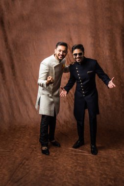 İki Hintli erkek etnik ya da geleneksel kıyafetler giyer, Sherwani ya da Kurta pijamalı erkek modeller, kahverengi grunge arka planında durup poz verirler, seçici bir odak noktası vardır.