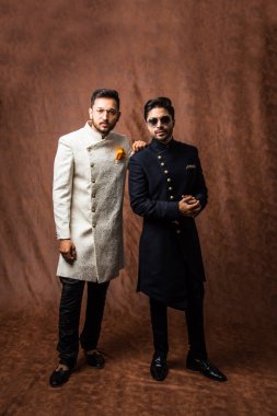 İki Hintli erkek etnik ya da geleneksel kıyafetler giyer, Sherwani ya da Kurta pijamalı erkek modeller, kahverengi grunge arka planında durup poz verirler, seçici bir odak noktası vardır.