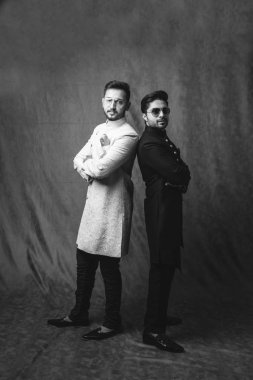 İki Hintli erkek etnik ya da geleneksel kıyafetler giyer, Sherwani ya da Kurta pijamalı erkek modeller, kahverengi grunge arka planında durup poz verirler, seçici bir odak noktası vardır.
