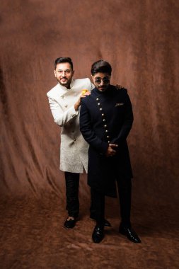 İki Hintli erkek etnik ya da geleneksel kıyafetler giyer, Sherwani ya da Kurta pijamalı erkek modeller, kahverengi grunge arka planında durup poz verirler, seçici bir odak noktası vardır.