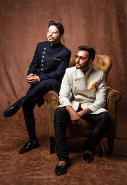 İki Hintli erkek etnik ya da geleneksel kıyafetler giyer, Sherwani ya da Kurta pijaması olan erkek modeller, kahverengi grunge arka planına karşı oturur ve kanepede poz verirler, seçici bir odak noktası vardır.