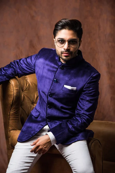 インドの男は 民族や伝統的な布を身に着けています 紫のコートと白いパンツとファッションモデル 茶色のグランジの背景にポーズ 選択的な焦点 — ストック写真