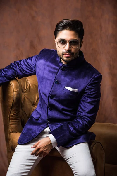 Indian Man wears ethnic or traditional cloths,  fashion model with purple coat and white pants, posing over brown grunge background, selective focus