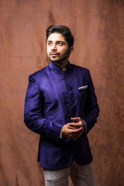 Indian Man wears ethnic or traditional cloths,  fashion model with purple coat and white pants, posing over brown grunge background, selective focus